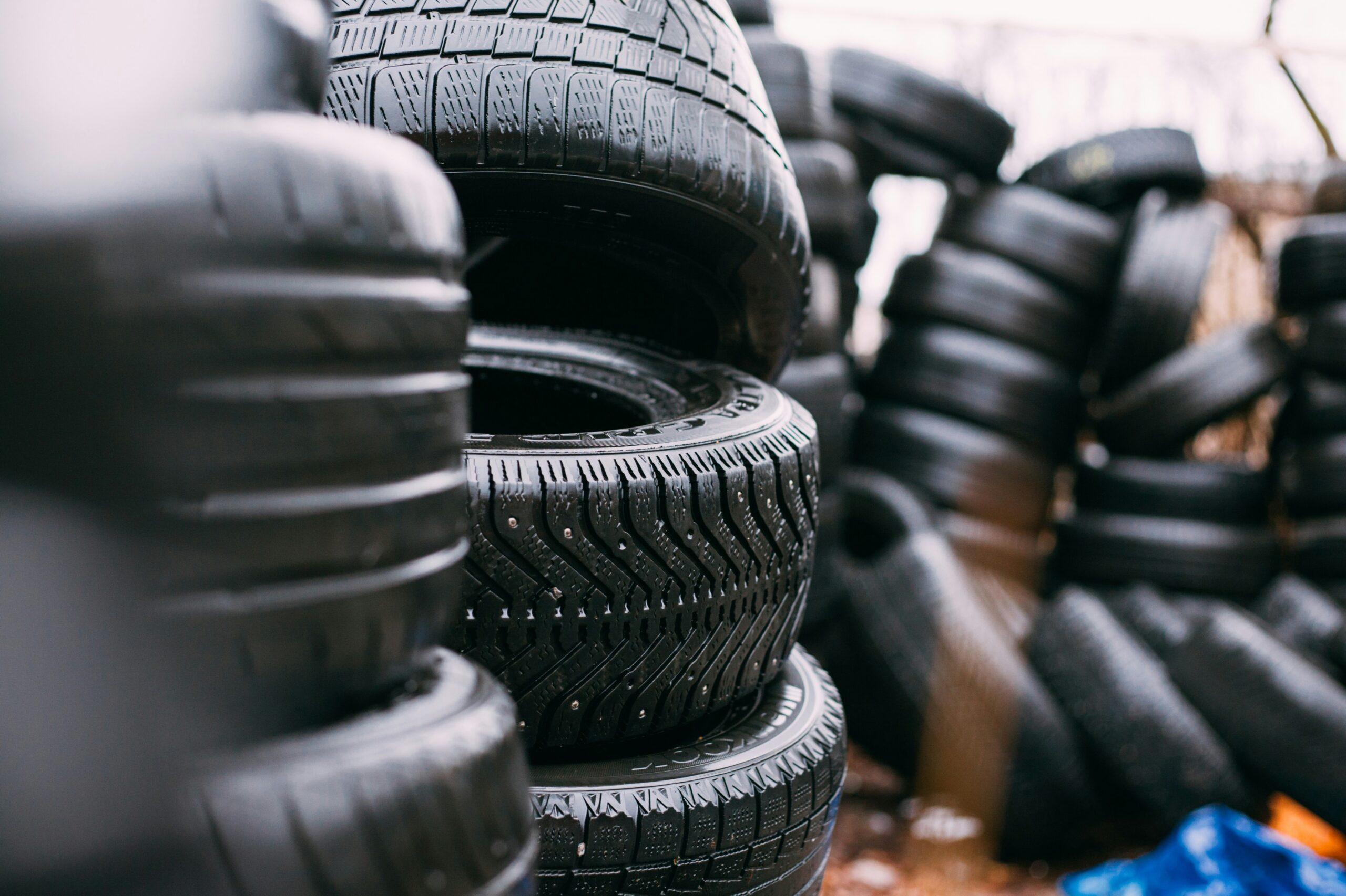Outdoor stacks of various tires piled on top of each other in a tire storage area.

